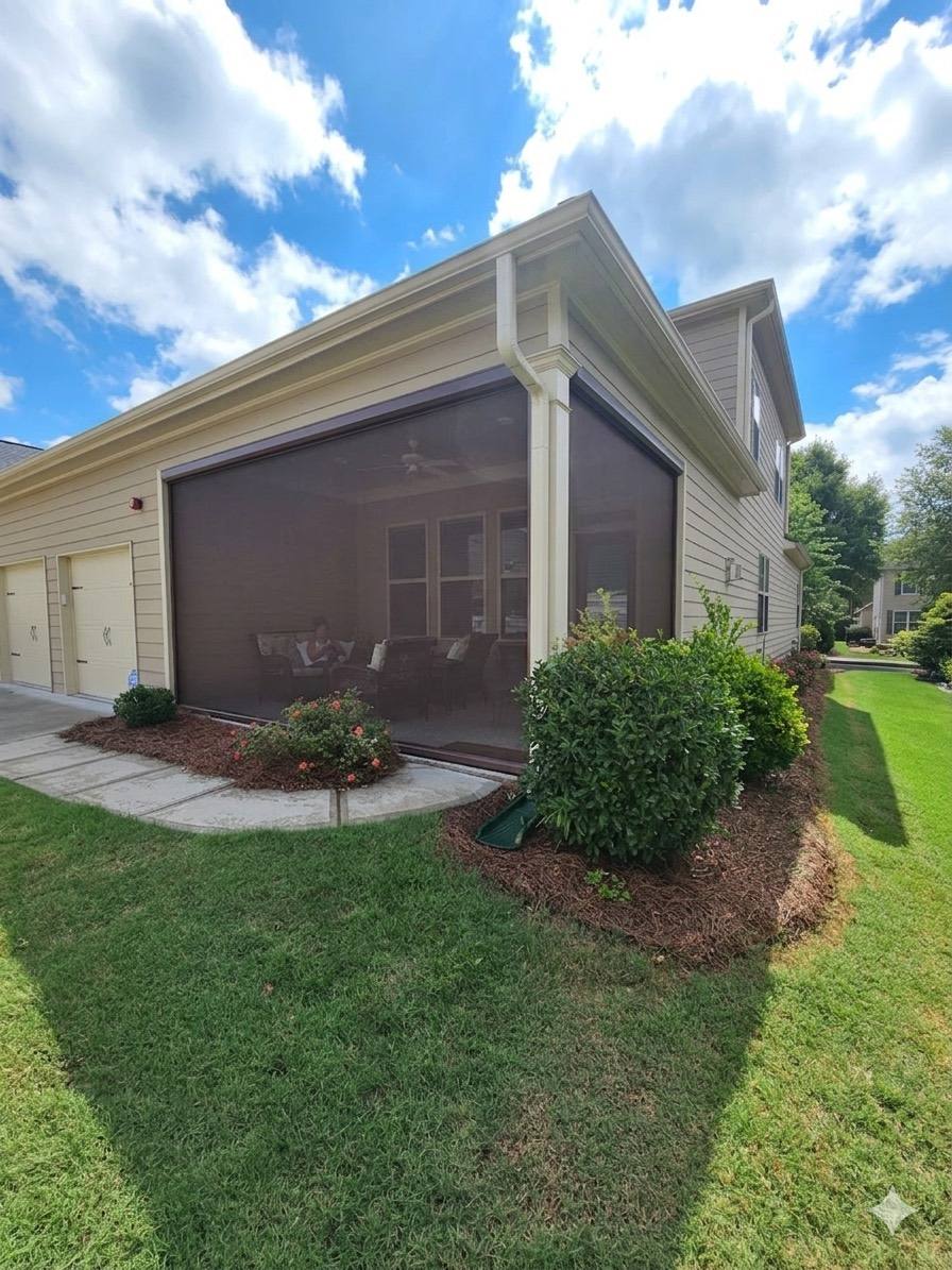 Fully lowered dark screens around a corner patio beside a landscaped lawn.