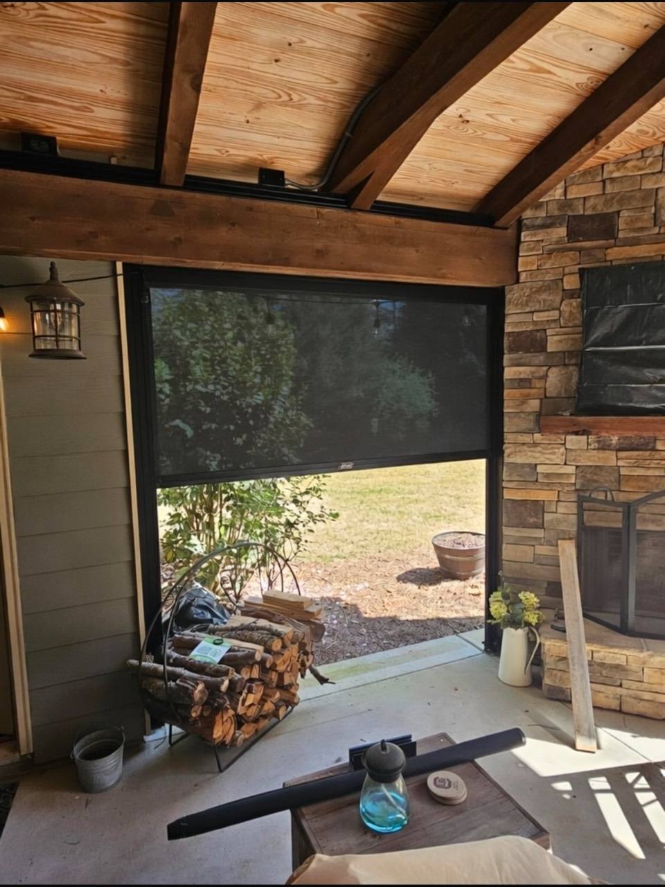 A partially lowered dark screen beside a stone fireplace beneath exposed timber beams.