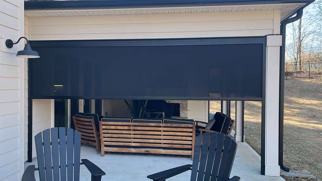 A wide dark screen partially lowered above wooden patio seating and Adirondack chairs.