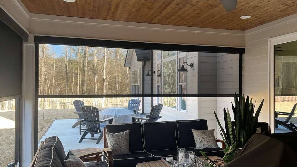 A furnished outdoor living room with a partially lowered screen facing a sunlit patio.