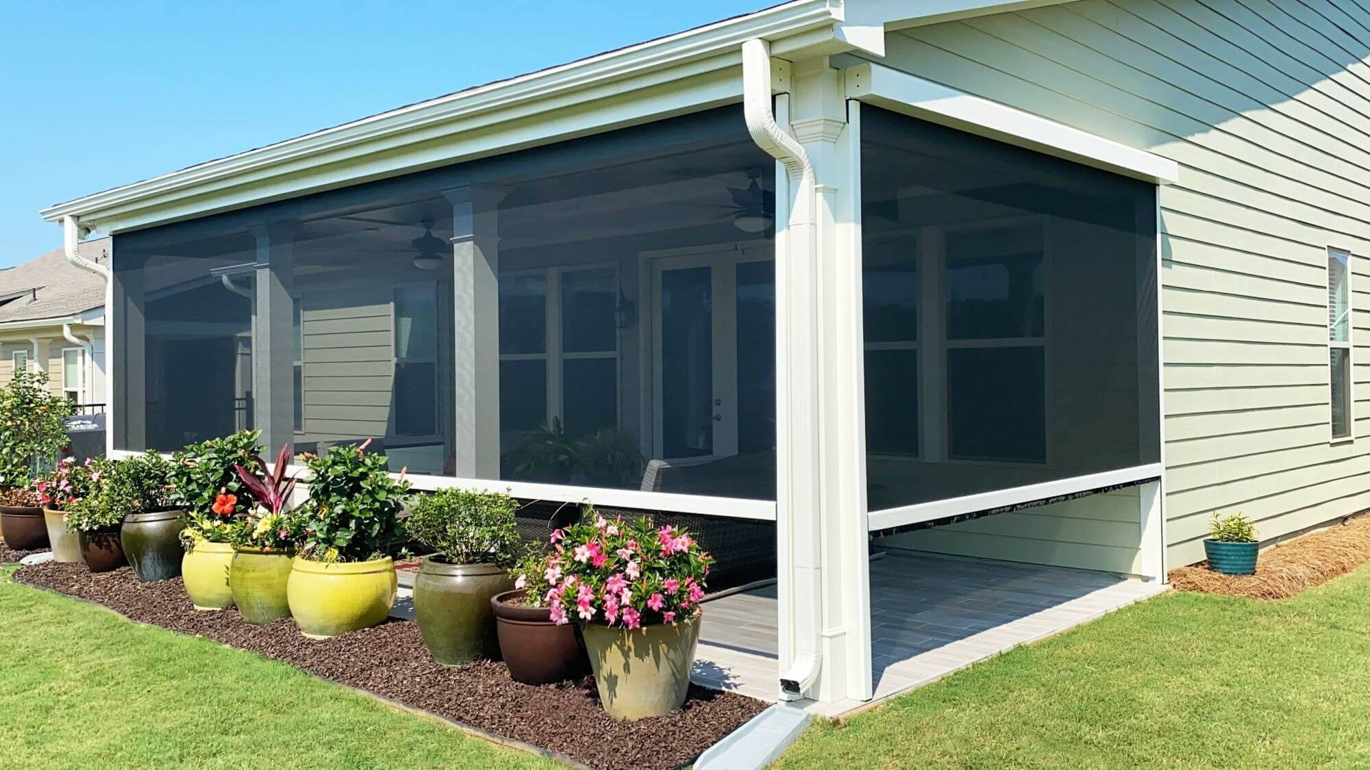 Dark solar screens along a light-colored garden patio with flowering plants outside.