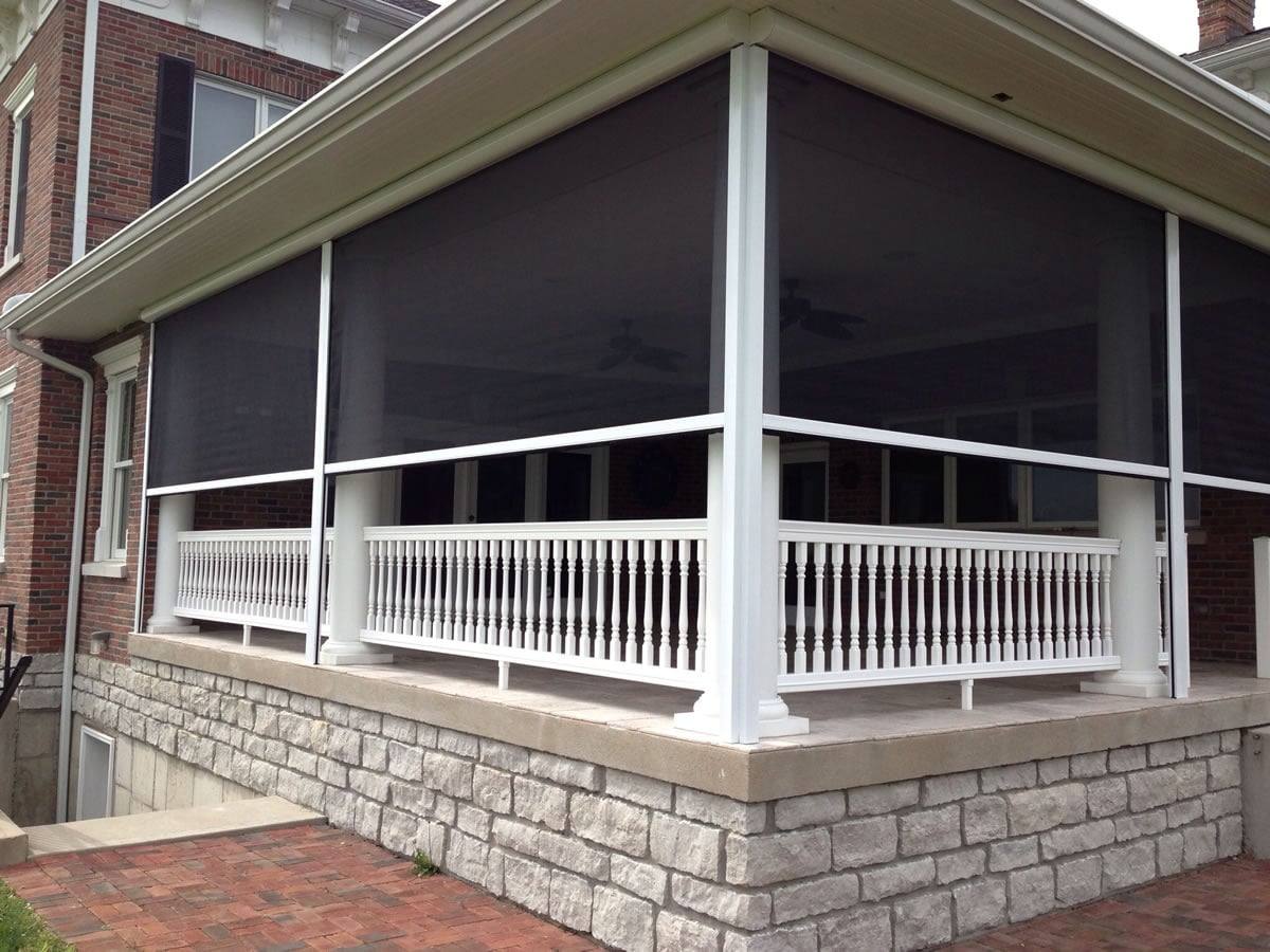 Partially lowered dark screens around a covered porch with white rails and stone foundations.
